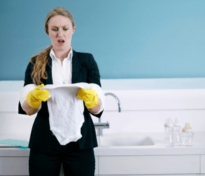 Mom with yellow rubber gloves holding a white baby onesie and looking shocked. This article asks and answers: is Dreft necessary.