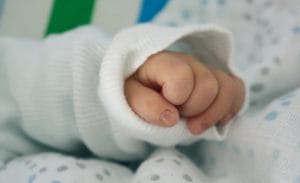 Baby's hand sticking out of the sleeve of a sweater. This article discusses what the bare minimum baby essentials are.