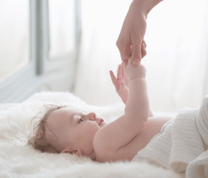 baby laying on bed holding parent's hand