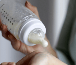 Person testing baby bottle temperature on wrist. This article discusses methods for preparing bottles for night feeds.