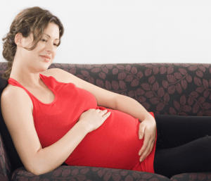 Pregnant woman in red sleeveless stop laying on a couch. This article share a twin birth story and disscusses what to expect at a twin pregnancy delivery.