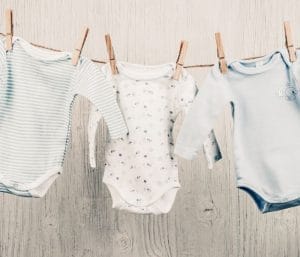 Baby onesies hanging on a clothing line. This post discusses how many baby clothes you need.