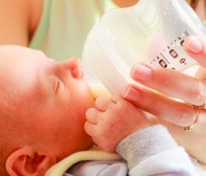 Newborn baby drinking from a bottle. This post discusses bottle feeding newborn baby tips.