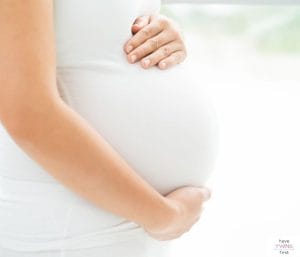 Woman holding pregnant belly. This article discusses what to expect when pregnant after twins.