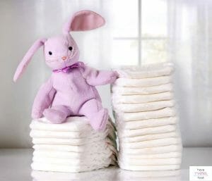 Diapers stacked in front of window with a stuffed bunny on top. This post discusses diaper blowout hacks and prevention.