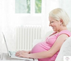 Pregnant woman looking at laptop. This post discusses when to start and share a baby registry.