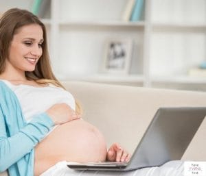 Pregnant woman looking at a laptop. This post reviews how to write a baby registry greeting.