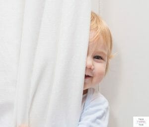 Baby hiding behind a curtain. This post covers the best blackout curtains available for the nursery.