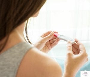 Woman looking at a pregnancy test. This article discusses twin pregnancy symptoms to expect at 6 weeks.
