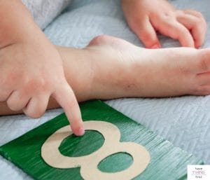 Baby pointing to a green and brown wooden number 8. This article reviews Montessori baby registry must haves.