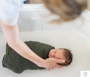 Mom putting her sleeping newborn in a bassinet. This article reviews how long to use a bassinet.