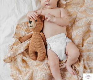Baby laying on blanket with a stuffed animal. This article reviews what to put on an eco-friendly baby registry.