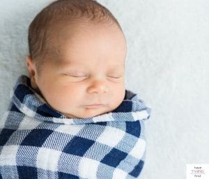 Baby asleep in a swaddle. This article answers the question how many swaddles, sleep sacks, and receiving blankets do I need?