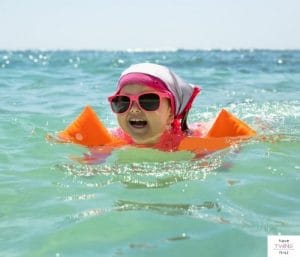 Toddler with puddle jumper and sunglasses swimming. This post discusses the best floaties for toddlers under 30 lbs.