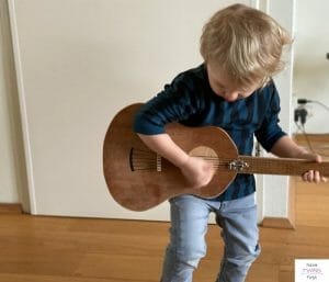 A child standing up and playing a guitar. This article reviews the best toddler guitars.