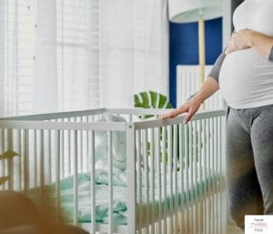 Pregnant woman in nursery with hand touching a crib. This articles discusses the best big ticket baby items.
