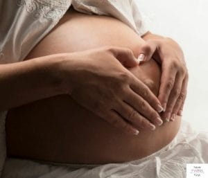 Expecting mom with both hands on pregnant belly. This article discusses how to announce your baby registry without a baby shower.