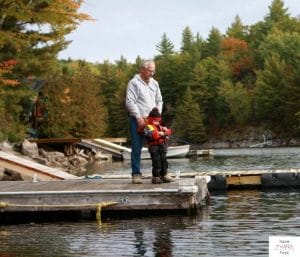 Grandfather with grandchild fishing on dock on a lake. This article discusses the best fishing poles for 3 year olds.
