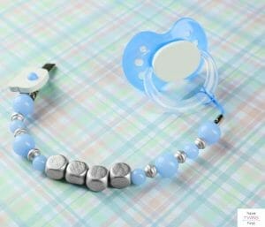 Pacifier attached to a pacifier clip laying on a crib sheet. This article discusses the most commonly forgotten baby registry items.