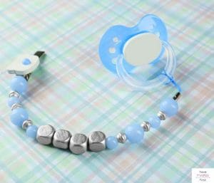Pacifier attached to a pacifier clip laying on a crib sheet. This article discusses the most commonly forgotten baby registry items.
