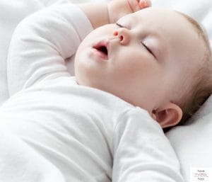 Baby with white long-sleeve onesie on and sleeping on back. This article discusses what to do when your baby is too big for a bassinet, but not ready for a crib.