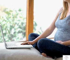 Pregnant woman sitting on a bed and looking at a laptop. This article is an Amazon baby registry review.