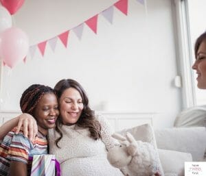 Women hugging and celebrating a baby shower. This article discusses how to share a baby registry.