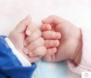 Two babies hands touching each other. This article discusses expectations for a newborn twins schedule.