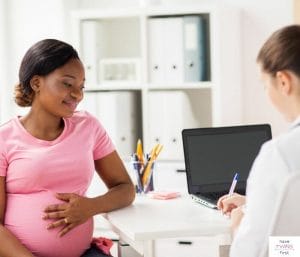 Pregnant mom sitting at desk and talking to a doctor. This article discusses what to expect at 24 weeks pregnant with twins.