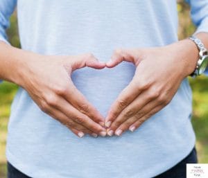 Woman making a heart shape with hands over her stomach. This article discusses what to expect at 10 weeks pregnant with twins.
