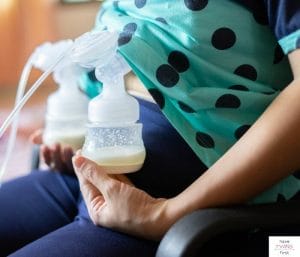 Mom sitting in office chair while pumping breast milk under shirt. This article reviews the the best pumping-friendly work clothes.