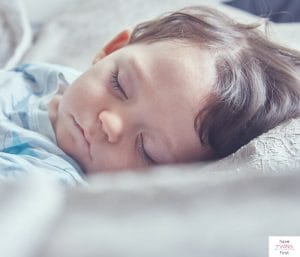 Toddler boy laying down and sleeping. This article discusses a typical 18 month old schedule for one nap.