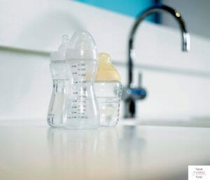 Baby bottles on kitchen counter next to a sink. This article answers the question: Can you put baby bottles in the dishwasher?