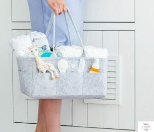 Woman standing and holding a diaper organizer. This article discusses what to put in a diaper caddy.