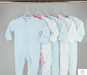Baby clothes hanging in a closet. This article asks how long do babies wear newborn clothes.