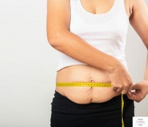 Postpartum mom measuring her waistline. This article discusses how to lose weight after twins.