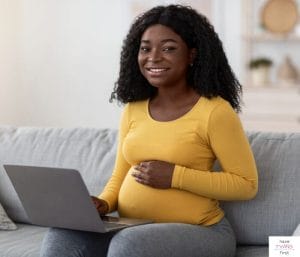 Pregnant woman sitting on couch with a laptop on her lap. This article talks about how what's included in a pregnancy spreadsheet template.