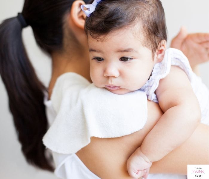 Mom burping baby over her shoulder. This article discusses the best baby burp cloths and bibs.